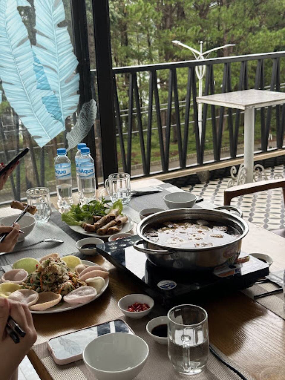 Nồi lẩu chay, gỏi và chả giò trên bàn cạnh cửa kính nhìn ra rừng thông