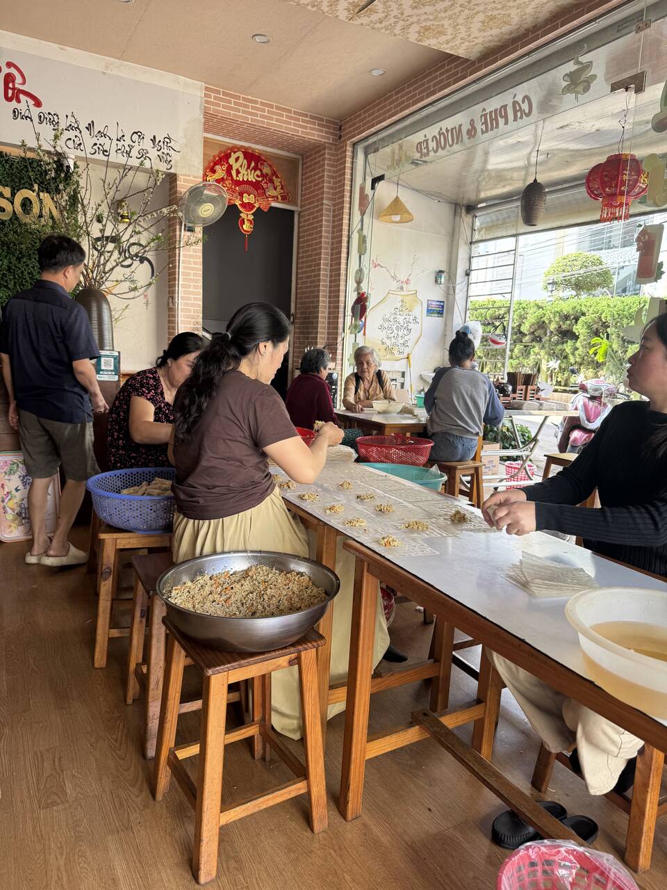 Mọi người ngồi quanh bàn, bày nhân và bánh tráng để cuốn chả giò trong Quán chay Vân Sơn