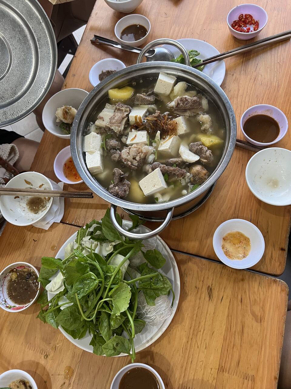 Nồi lẩu bò nấm với đậu phụ, thịt và đĩa rau sống trên bàn gỗ