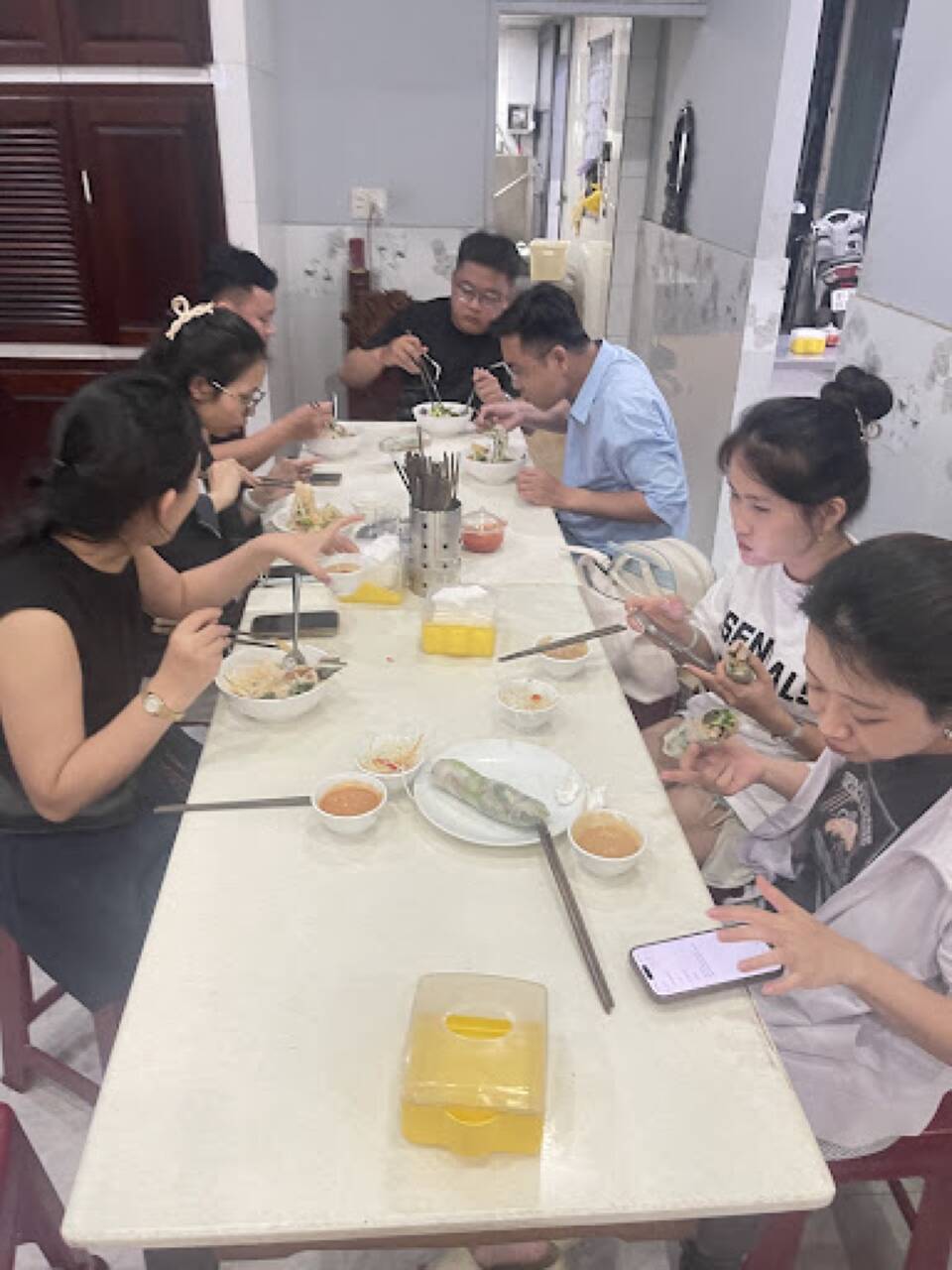 Bàn dài khách ngồi ăn trong quán Bún Phương, có hộp đựng đồ ăn kèm trên bàn