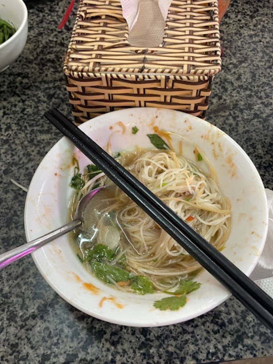 Bát phở nước với bún, rau thơm và đĩa giá đỗ trên bàn đá tại Phở Ngọc Sơn