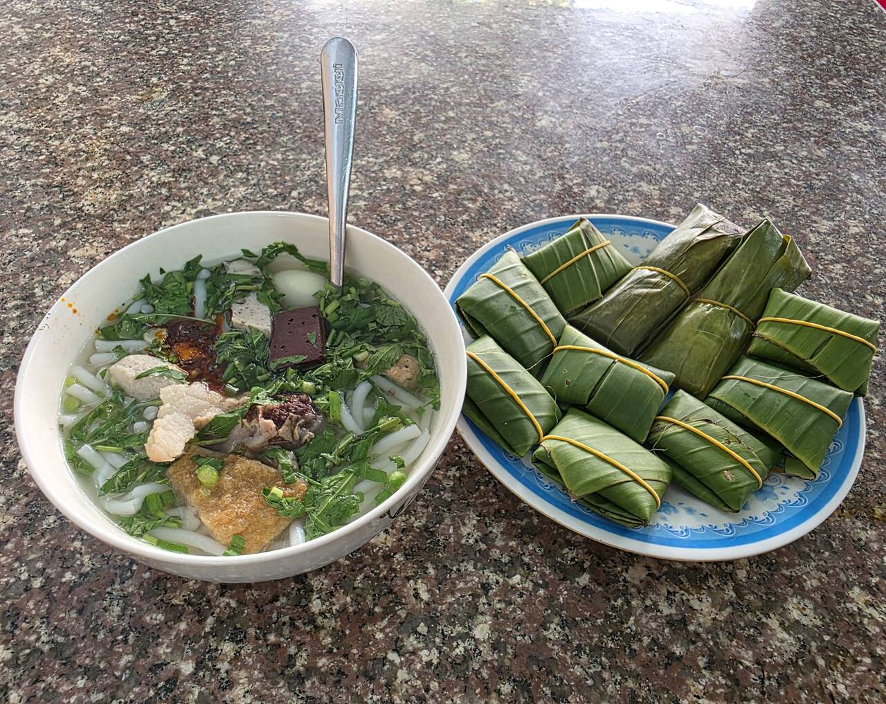 Tô bánh canh rau xanh, thịt và chả cạnh đĩa nem gói lá chuối trên mặt bàn đá tại Quán Bánh Canh 32
