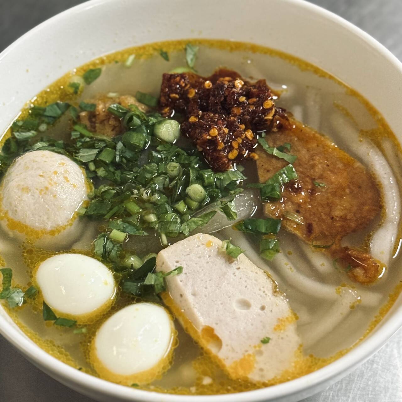Tô bánh canh nước trong có viên, chả, trứng cút và sa tế tóp mỡ ở Bánh Canh Cô Bông