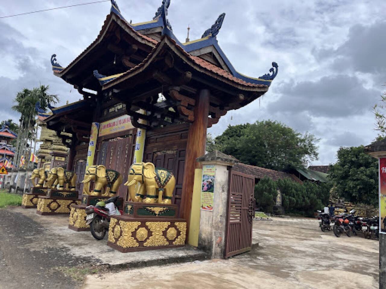 Cổng gỗ mái cong của chùa Bửu Minh với hàng voi vàng trước cổng