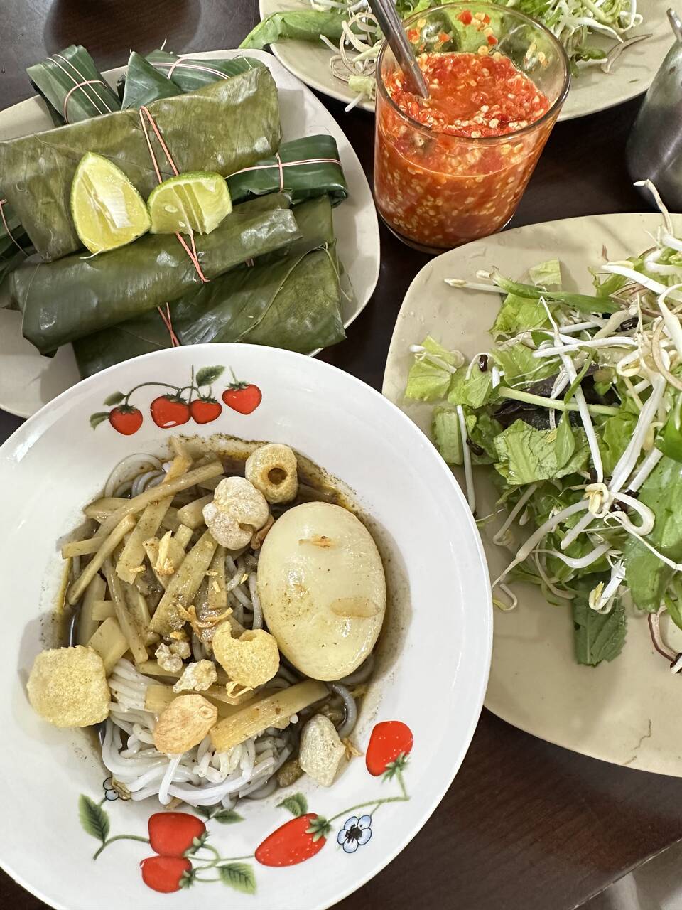 Tô bún cua nước đen có trứng, măng và tóp mỡ, kèm nem gói lá, rau sống và chén ớt tại Bún cua Chi
