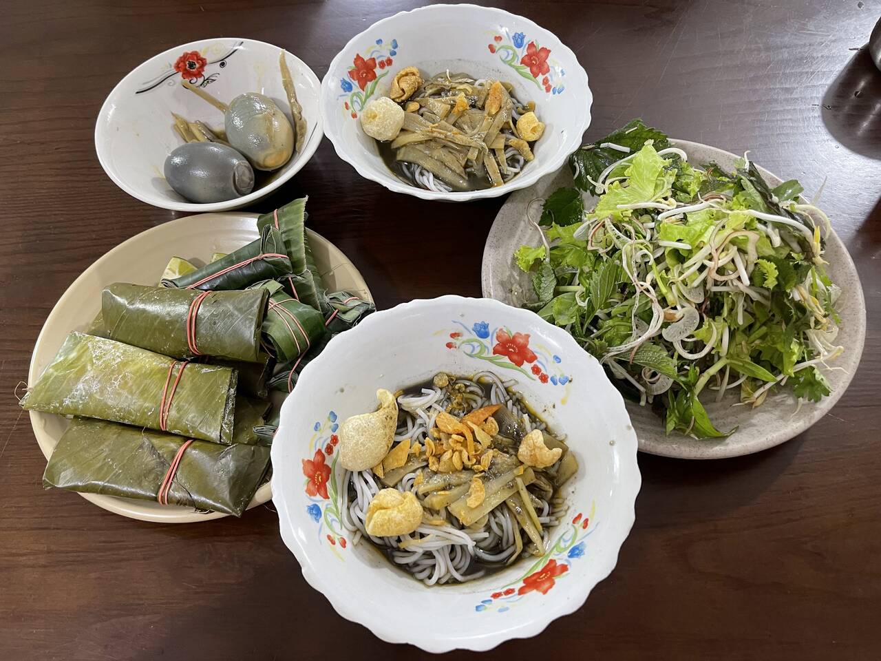 Hai tô bún cua thối, đĩa rau sống, nem gói lá và trứng trên bàn gỗ tại Bún cua Chi