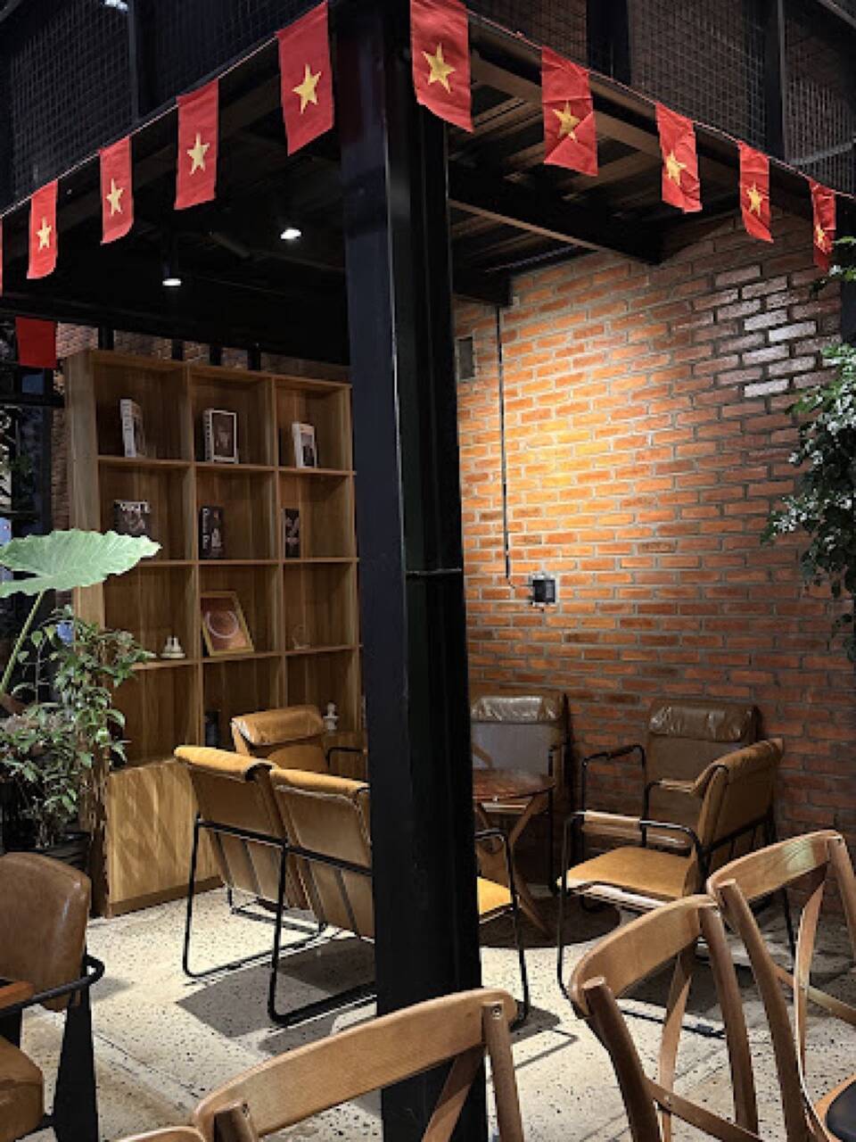 Góc ngồi trong quán The Quao với tường gạch, kệ sách và ghế gỗ