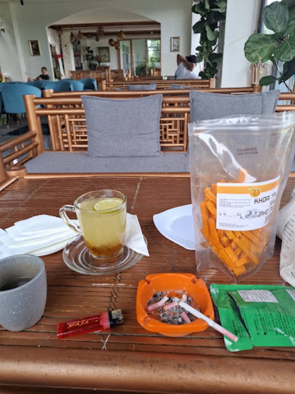 Bàn ngồi trong quán The Wind Coffee có ly trà chanh và túi đồ ăn vặt, khu ghế sofa phía sau
