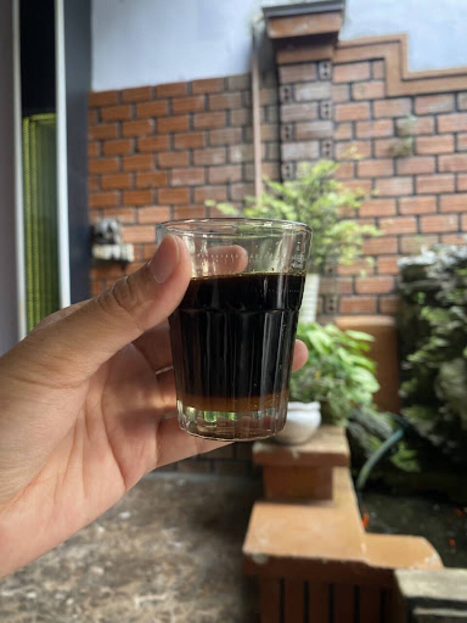 Ly cà phê đen pha phin được cầm trên tay cạnh bức tường gạch tại Cafe Thu Hà