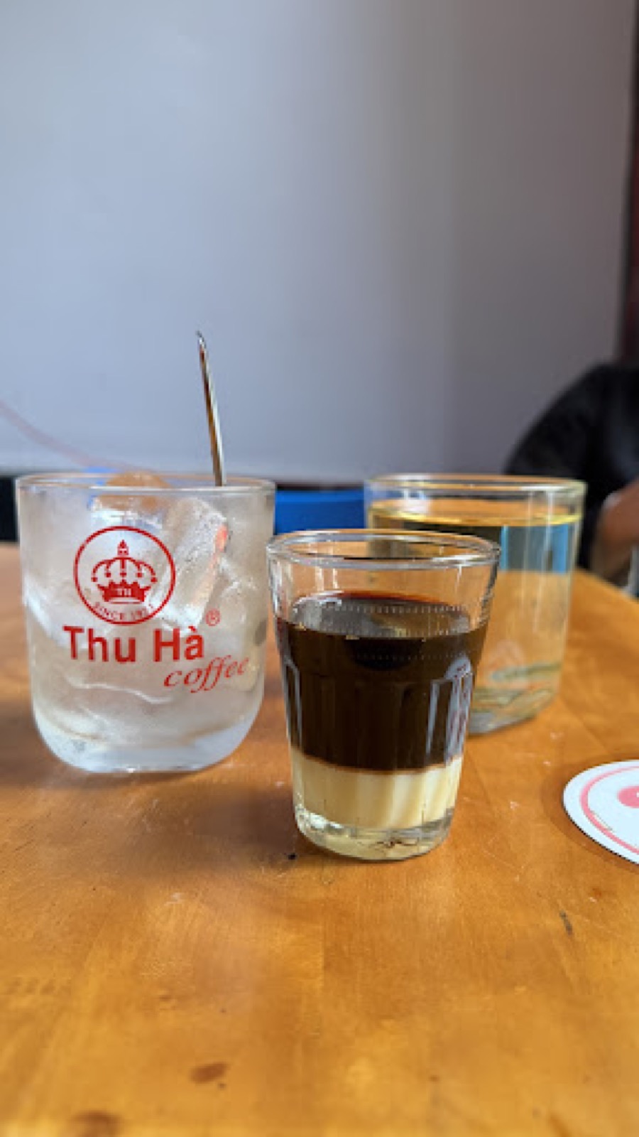 Ly cà phê đen và ly nước có logo Thu Hà trên bàn gỗ