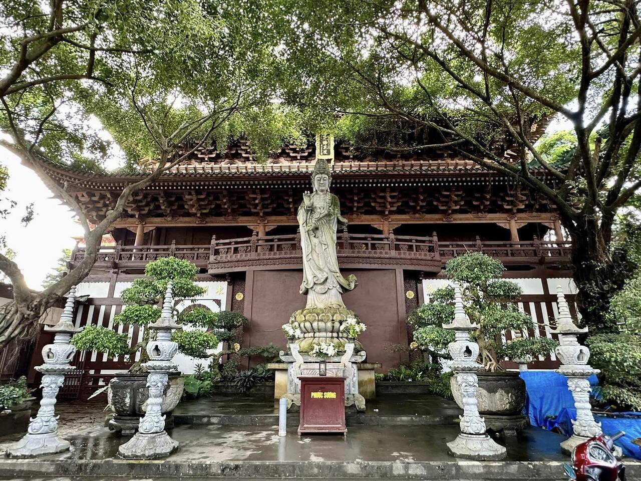 Tượng Quan Âm đứng trước chánh điện, hai bên là bình bonsai và cột đá