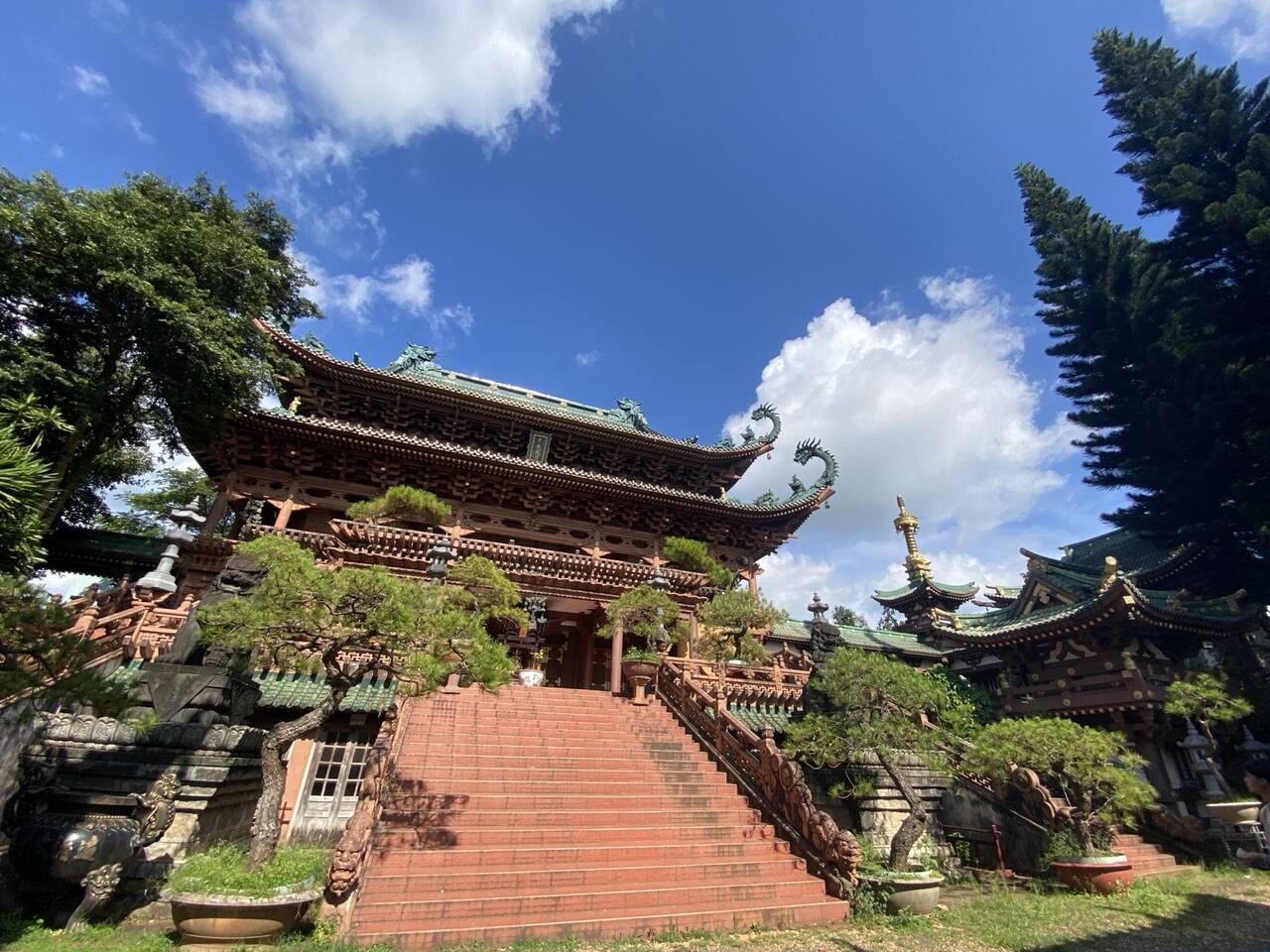 Bậc thang đá đỏ dẫn lên chánh điện mái cong, cây bonsai hai bên