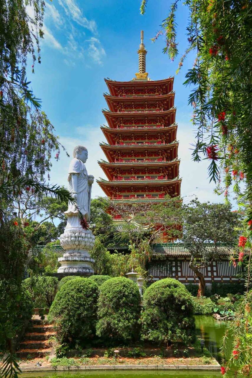 Tháp đỏ nhiều tầng mái nhọn vàng đứng sau tượng Phật trắng trên đài sen ở chùa Minh Thành