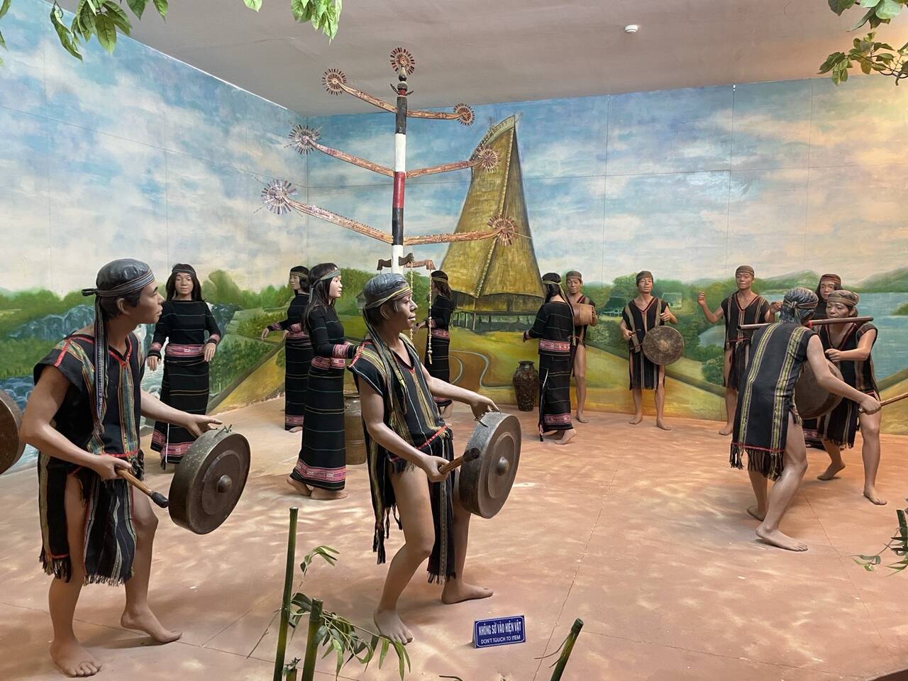 Mô hình nghệ nhân đánh cồng chiêng và các cô gái đứng thành vòng trong gian trưng bày của bảo tàng