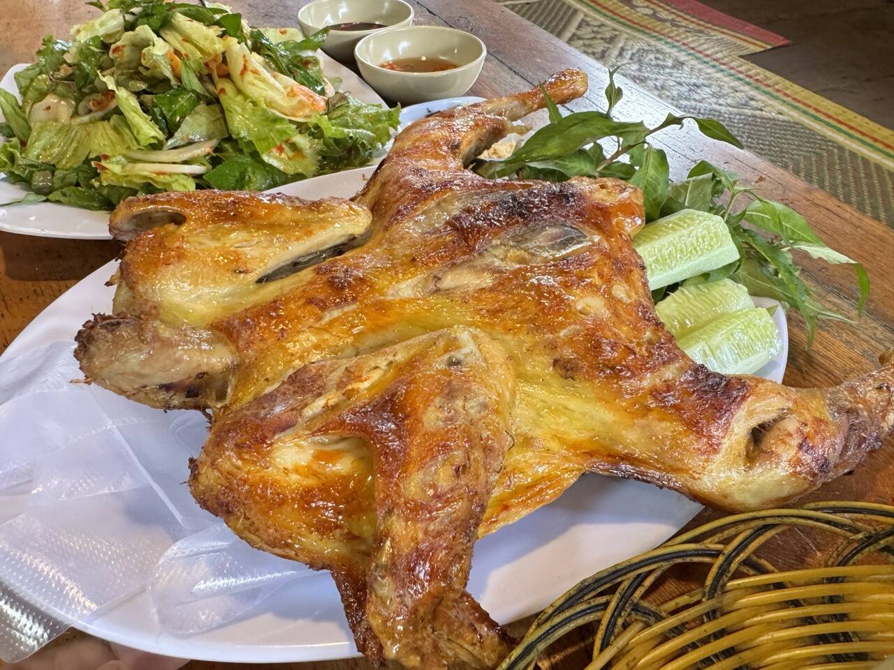 Gà nướng nguyên con vàng sẫm trên đĩa, kèm rau thơm và dưa leo tại Plit
