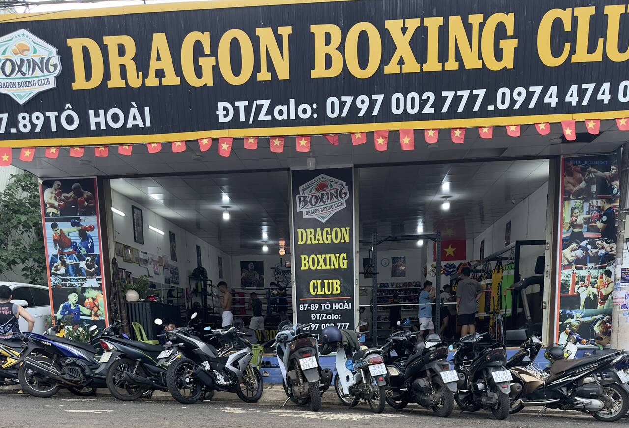 The front of Dragon Boxing Club at 87-89 Tô Hoài, with a black sign in gold lettering and motorbikes parked outside