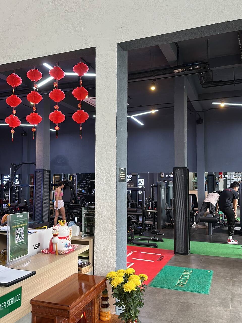 The Power Fitness Center reception desk with red lanterns, a welcome mat and a row of machines behind