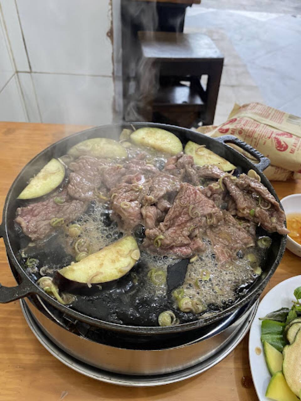 A steaming cast-iron pan of grilled beef with aubergine at Anh Chín