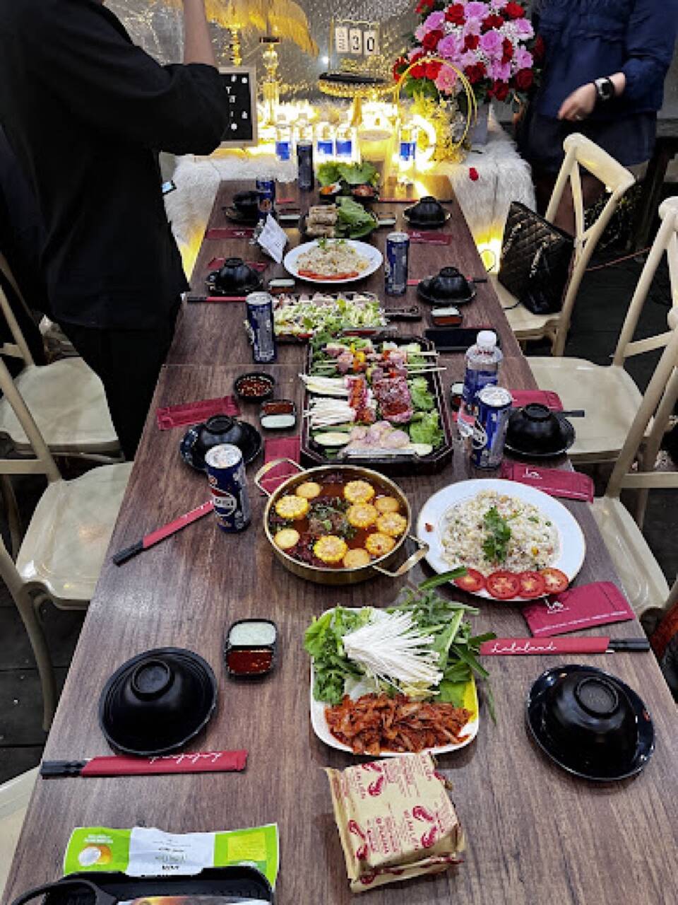 A long group table with hotpot, fried rice and a grill tray at La La Land