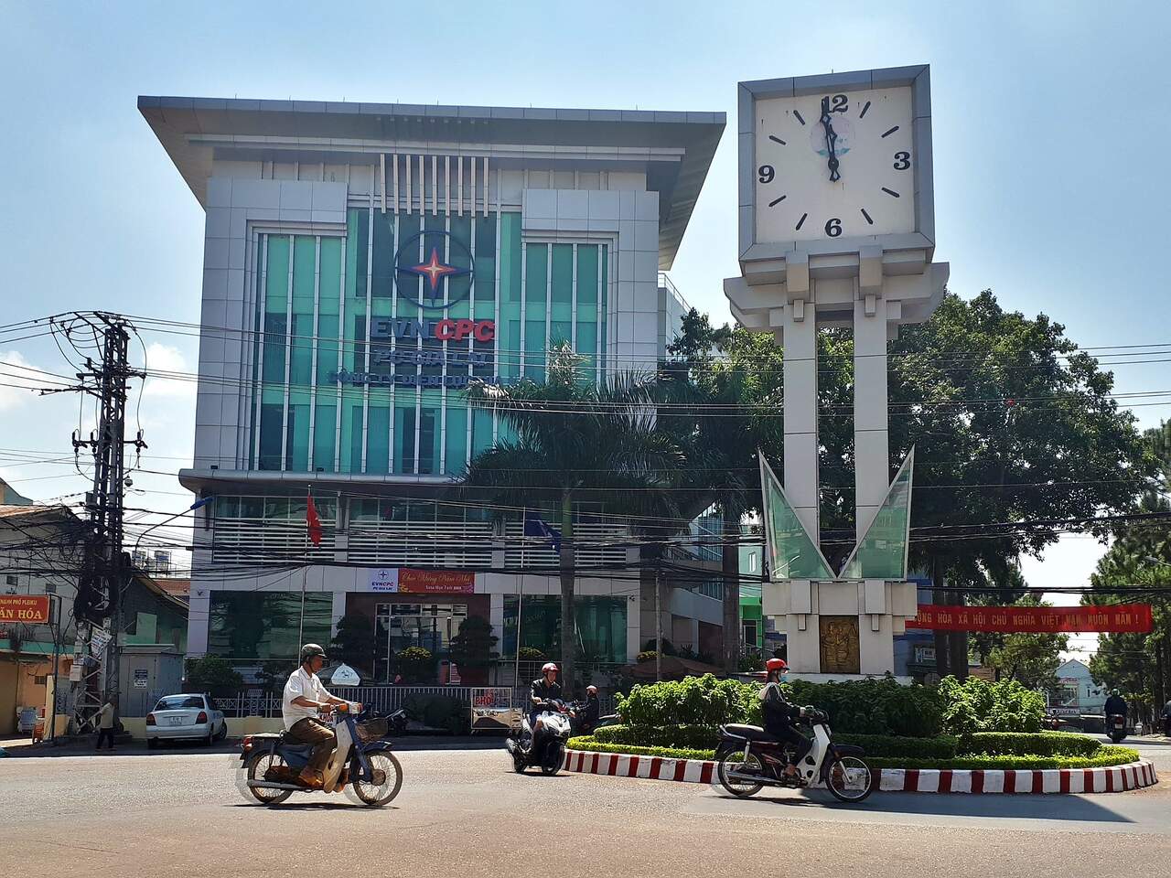 Tòa nhà kính nhiều tầng có logo EVNCPC cạnh tháp đồng hồ ở vòng xoay