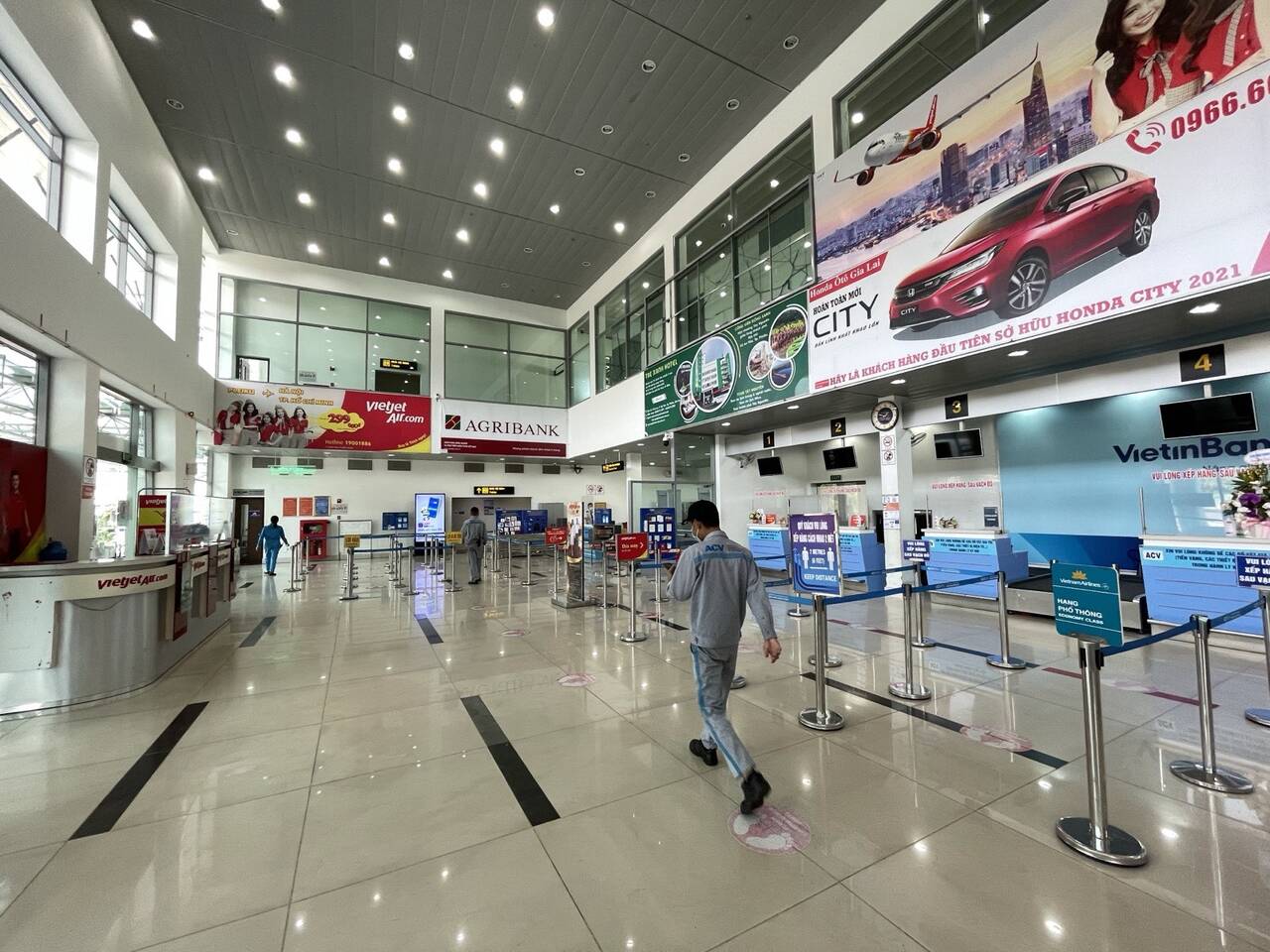 Sảnh làm thủ tục với quầy đánh số 1 đến 4, quầy Vietjet và Vietnam Airlines, nhân viên mặc đồng phục xám đi qua