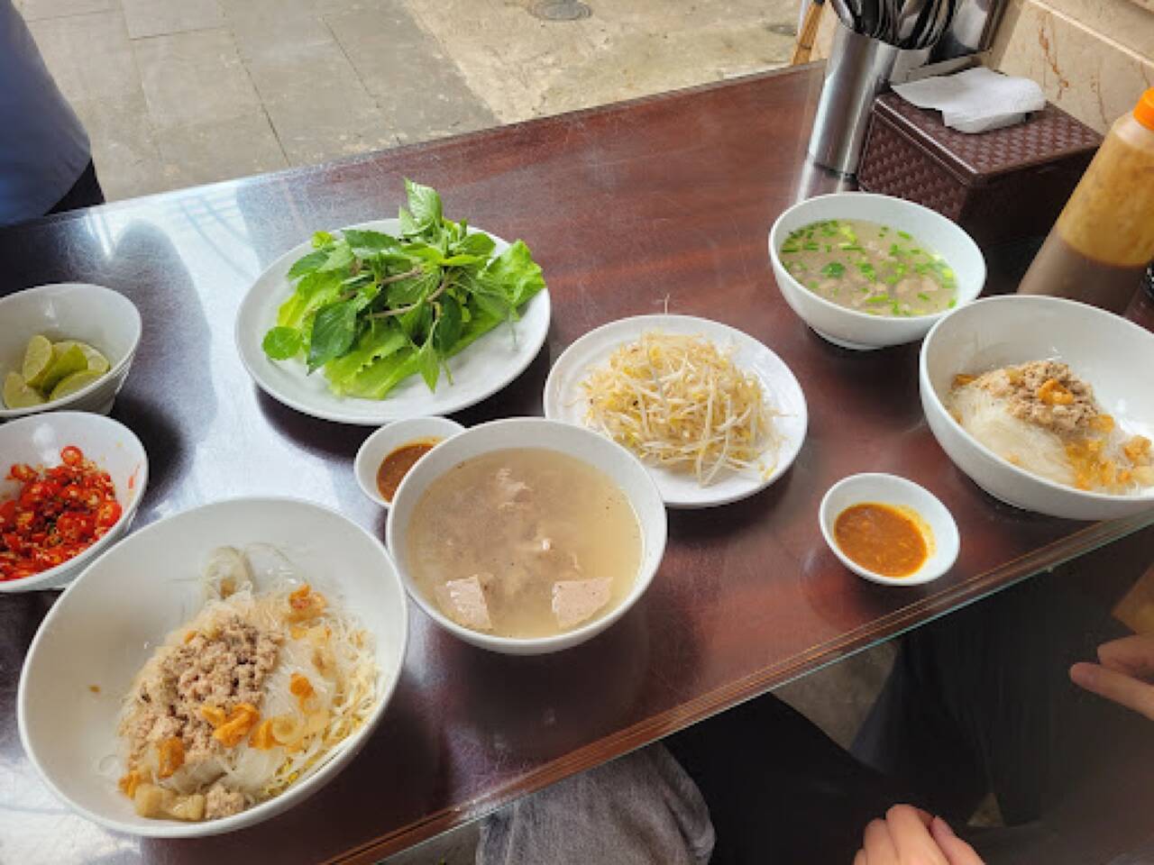 Hai bát phở khô trộn thịt băm, bát nước dùng, đĩa rau sống và giá đỗ trên bàn tại Phở khô Hồng