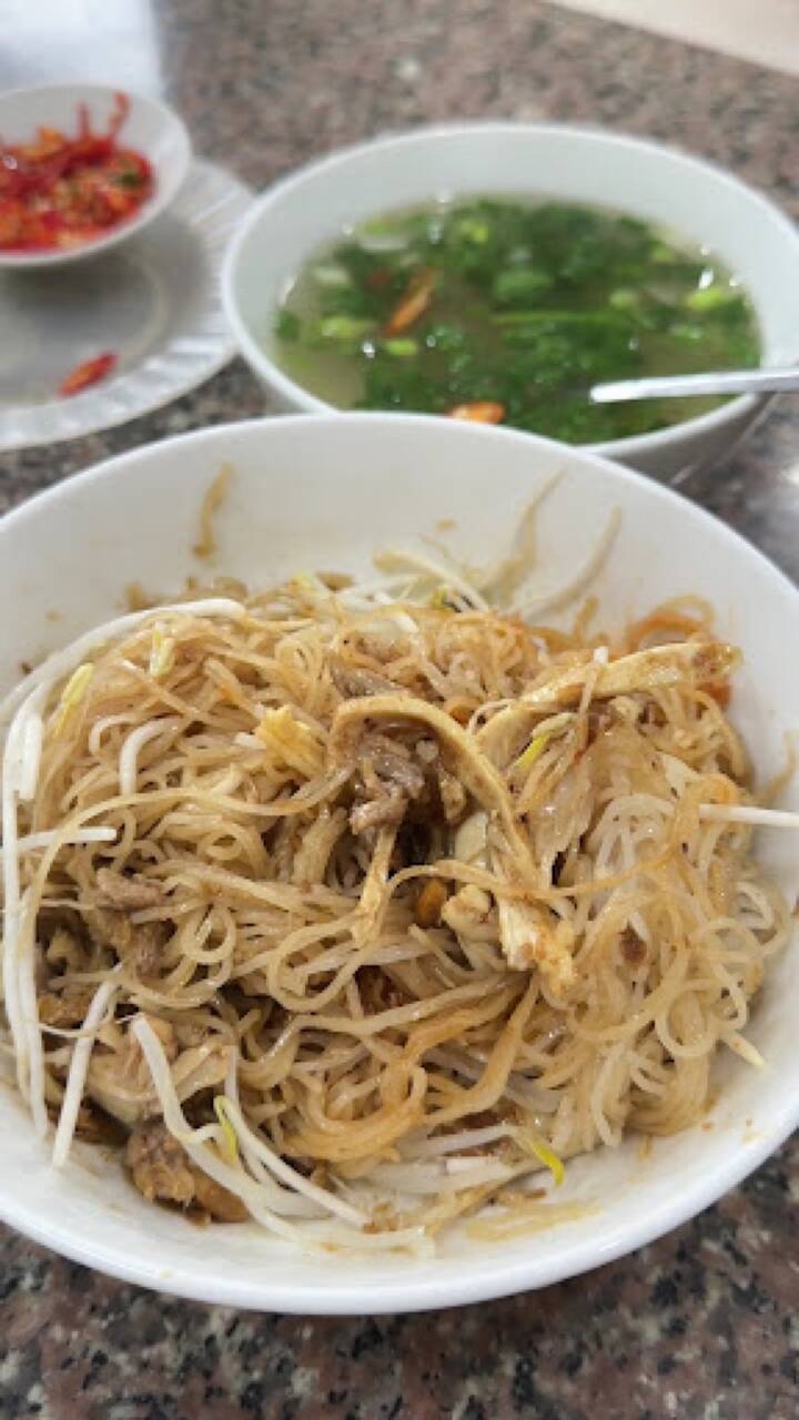 Bát phở khô trộn với giá đỗ và bát nước dùng rau hành trên bàn đá tại Hùng Ròm